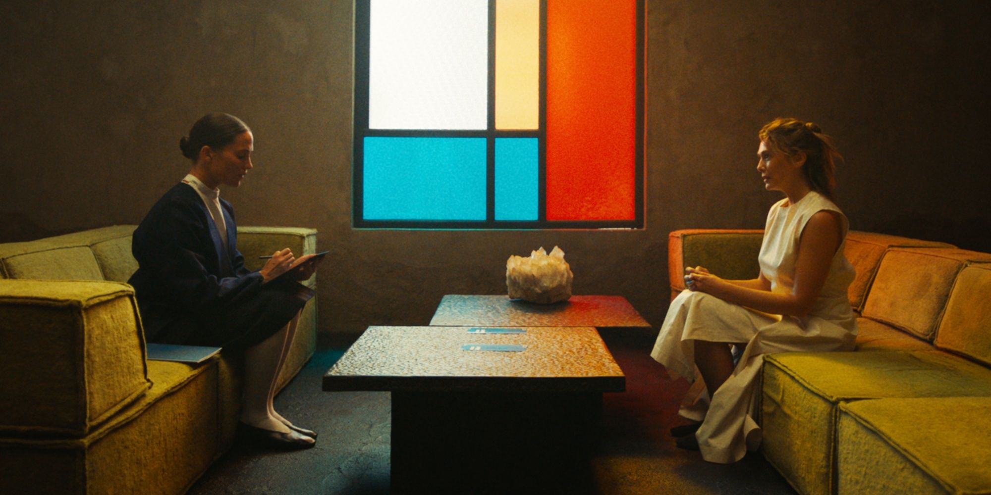 Elizabeth Olsen as Mia sitting on a couch opposite Alicia Vikander as Virginia in The Assessment
