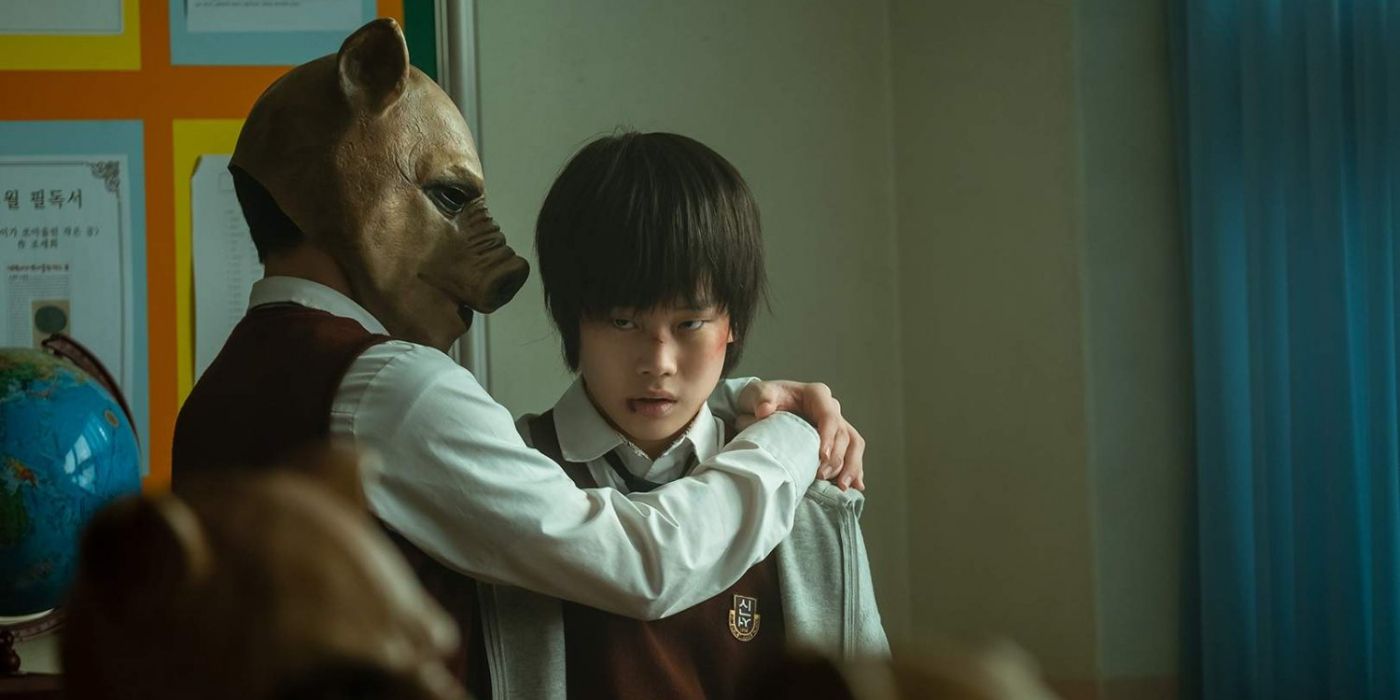 A man wearing a pig mask on the left is holding a young man on the right and talking into his ear in the K-drama The King of Pigs