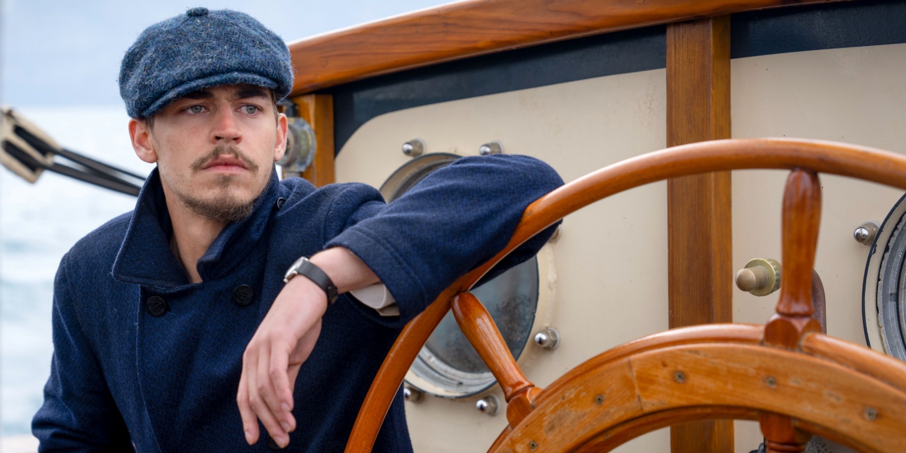 Hero Fiennes Tiffin as Henry Hayes leaning on the wheel of a ship in The Ministry of Ungentlemanly Warfare