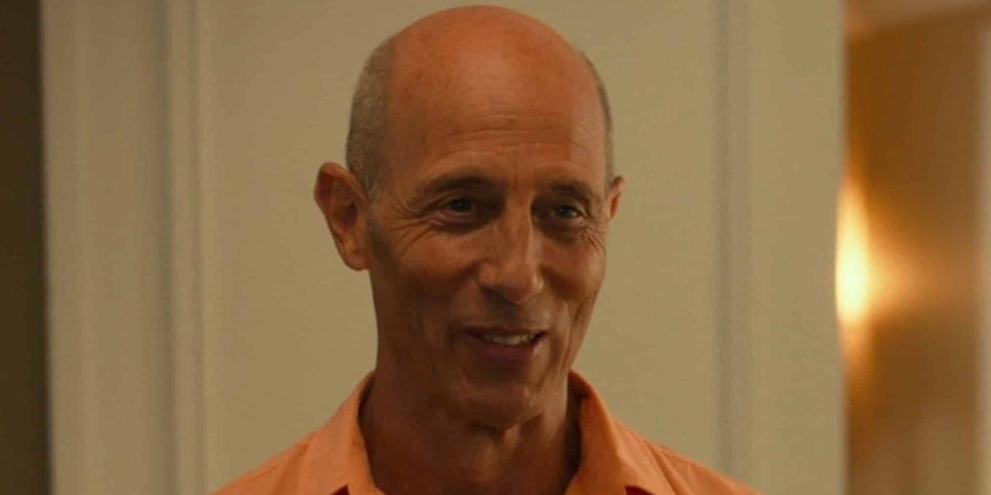 A man in an orange shirt looks at someone off-camera in The White Lotus.