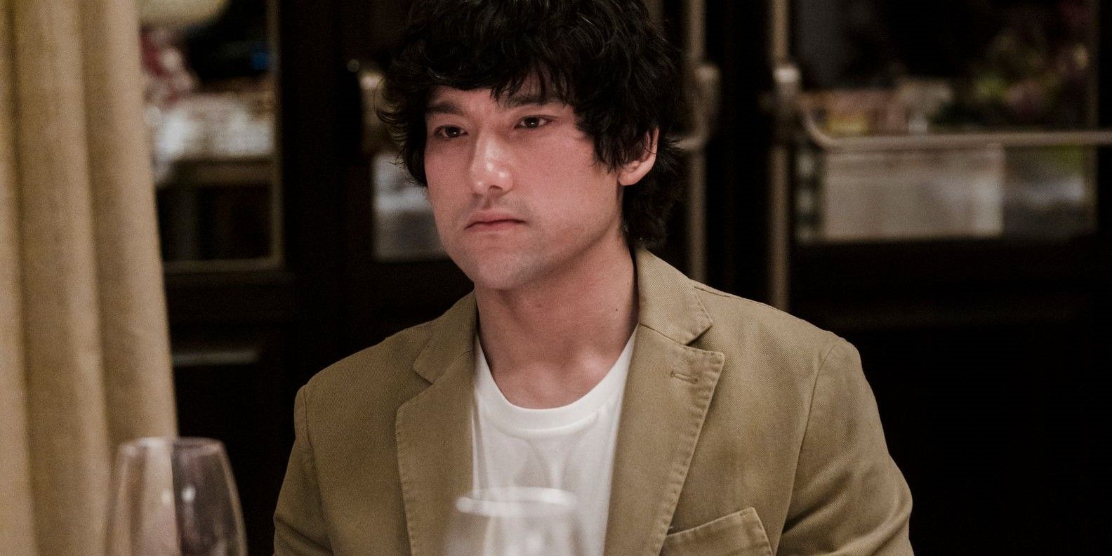 Will Sharpe as Ethan Spiller sits at a dinner table and looks serious in The White Lotus Season 2.