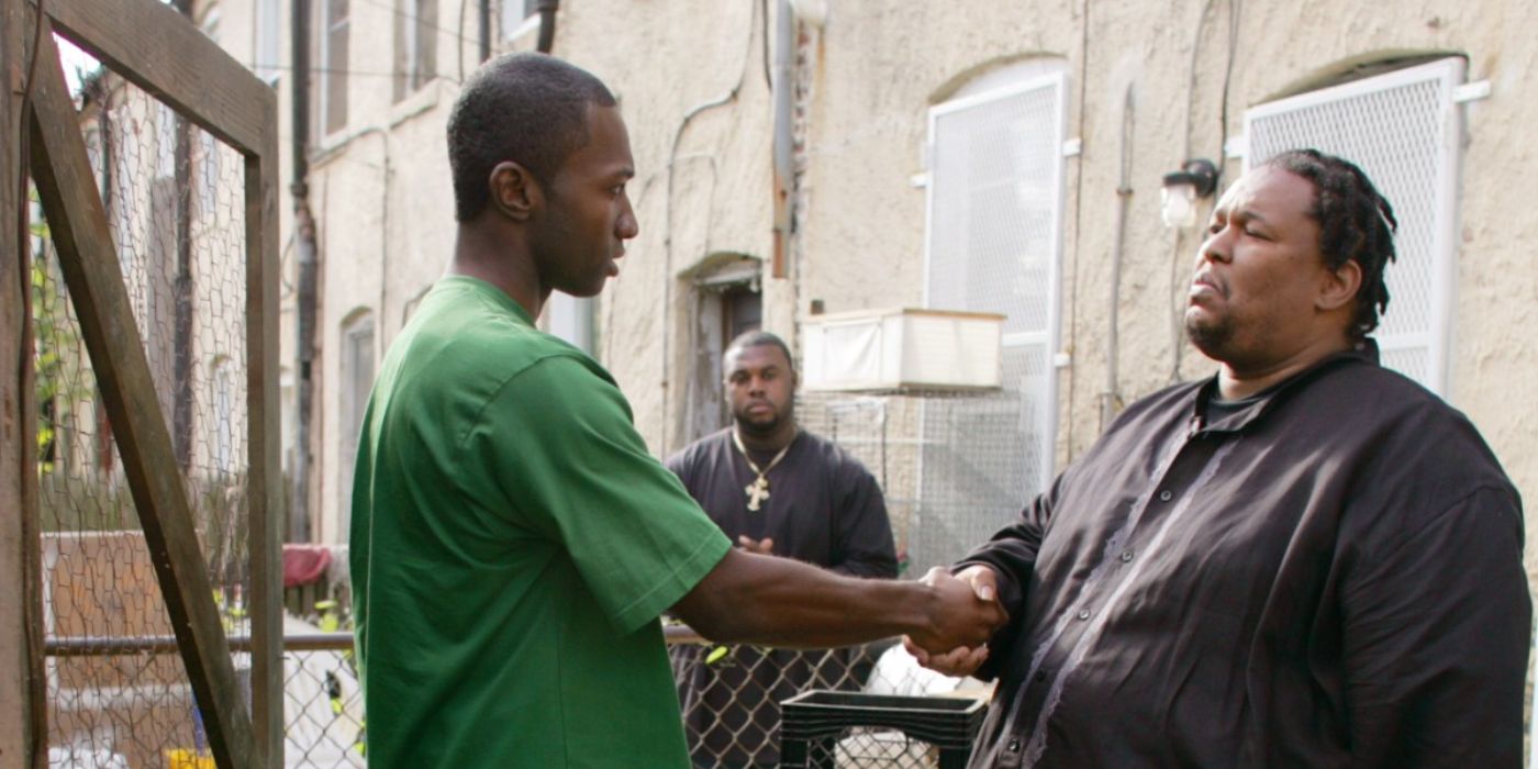 Two men shake hands in an alley as a third watches in The Wire.