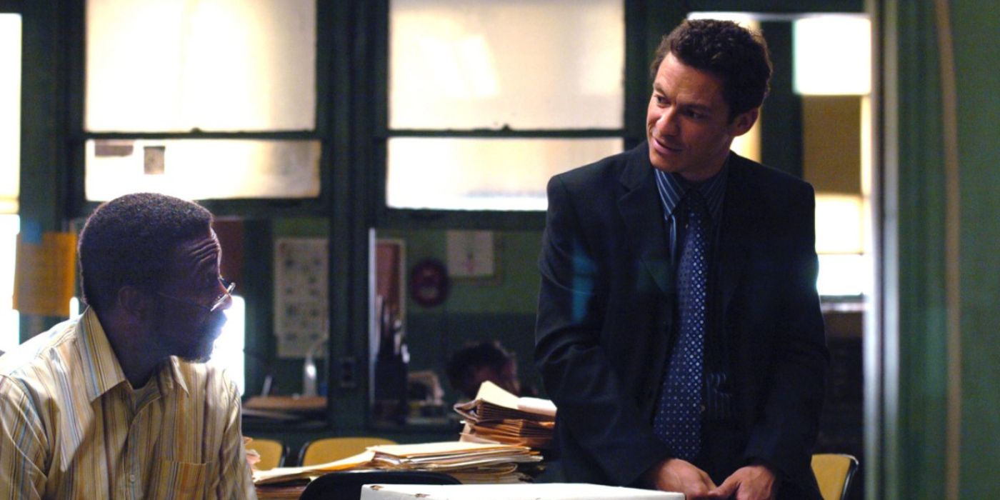 Two men in business clothing talk, sitting at and on a desk in The Wire.