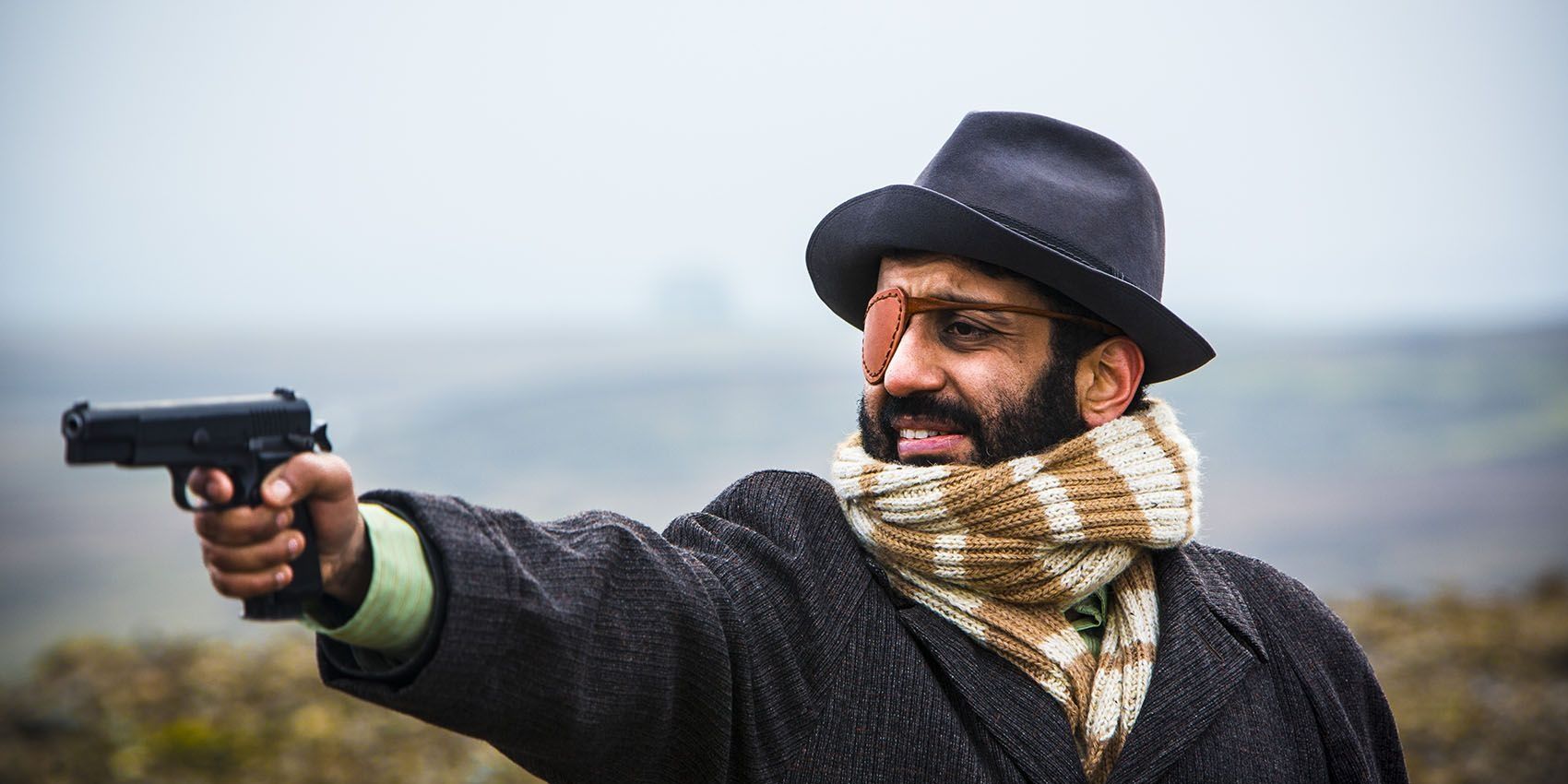 Adheel Akhtar as Wilson Wilson in Utopia holding a gun.