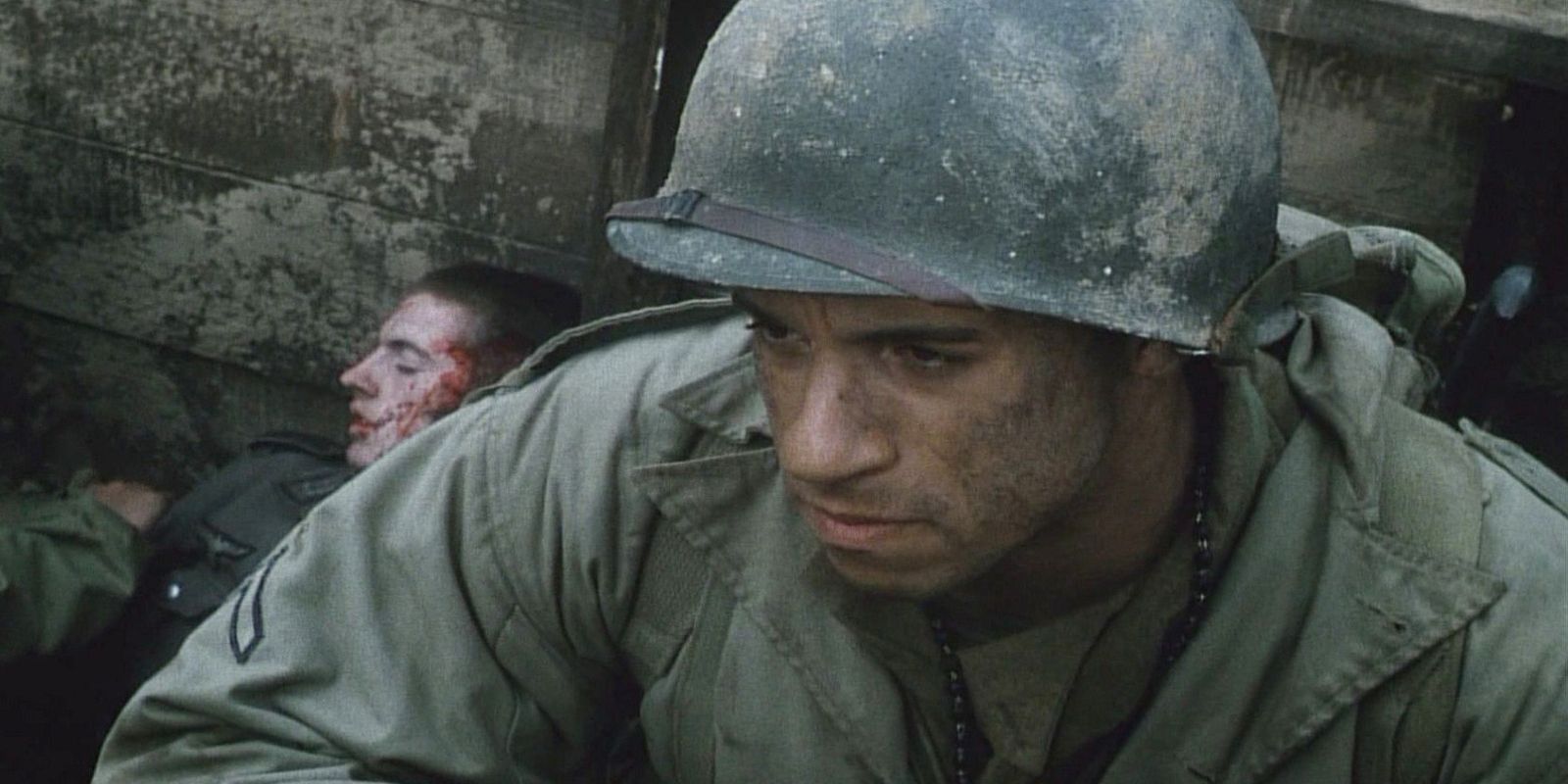 Vin Diesel as a soldier, covered in mud, with an injured person behind him in Saving Private Ryan.