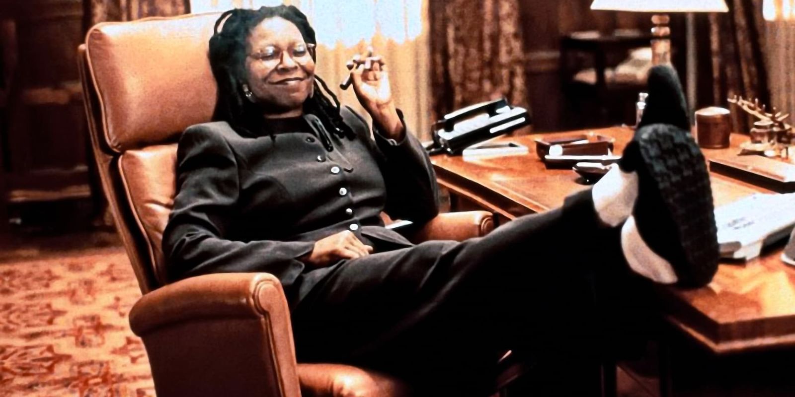 Whoopi Goldberg leaning back on a chair with her feet up on a desk in The Associate