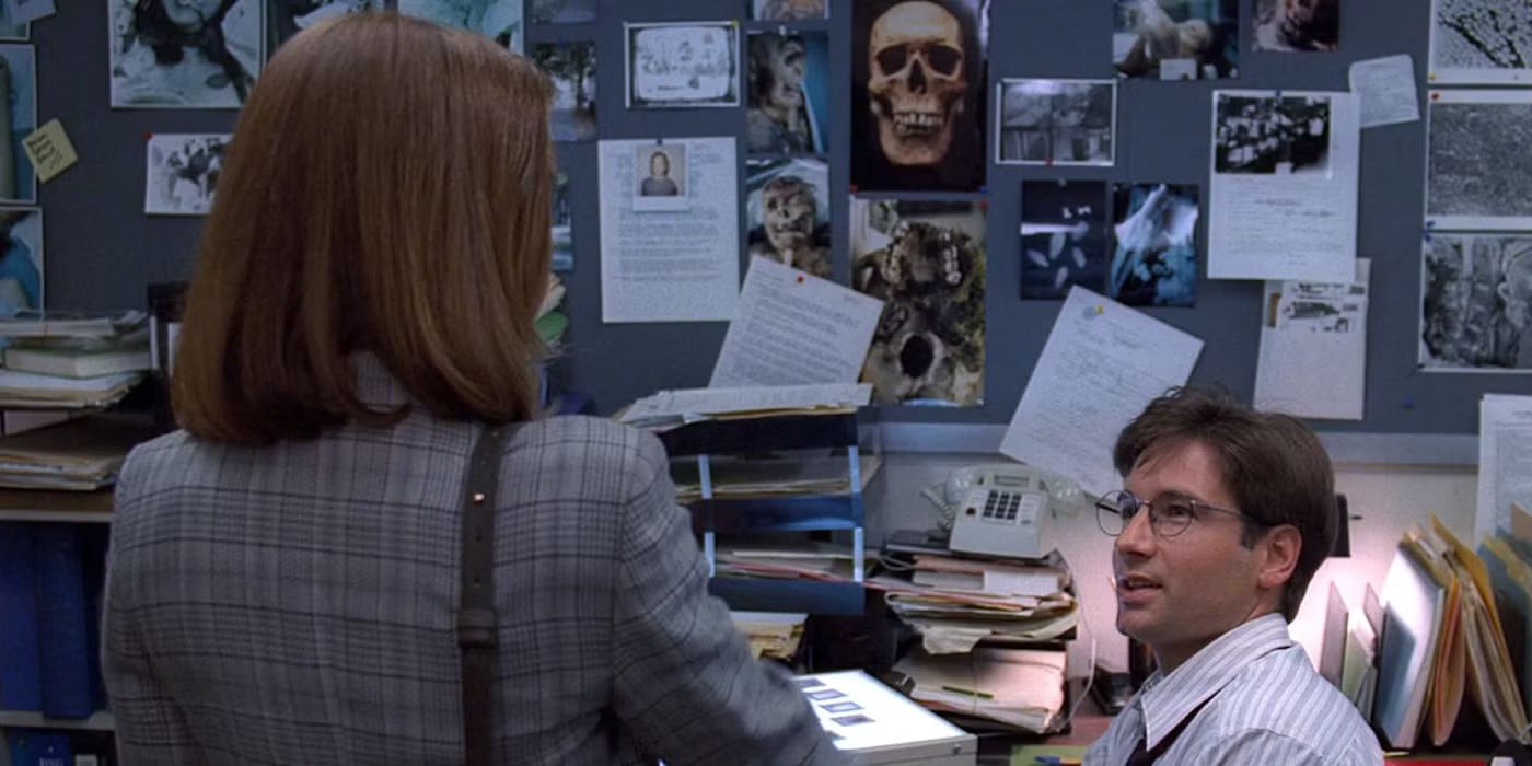 Agents Mulder and Scully talk near a cluttered workstation in The X-Files.