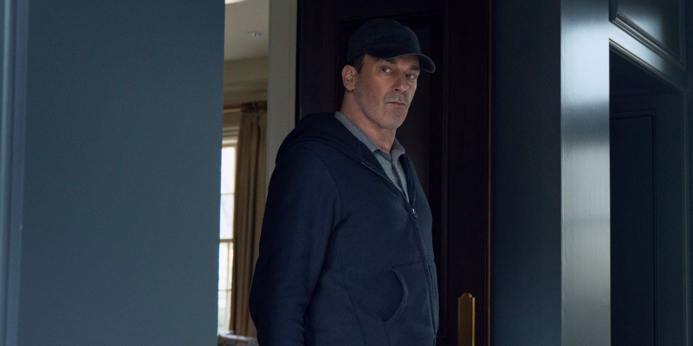 Jon Hamm, wearing a baseball cap and gray hooding, while sneaking inside a home in Your Friends and Neighbors.