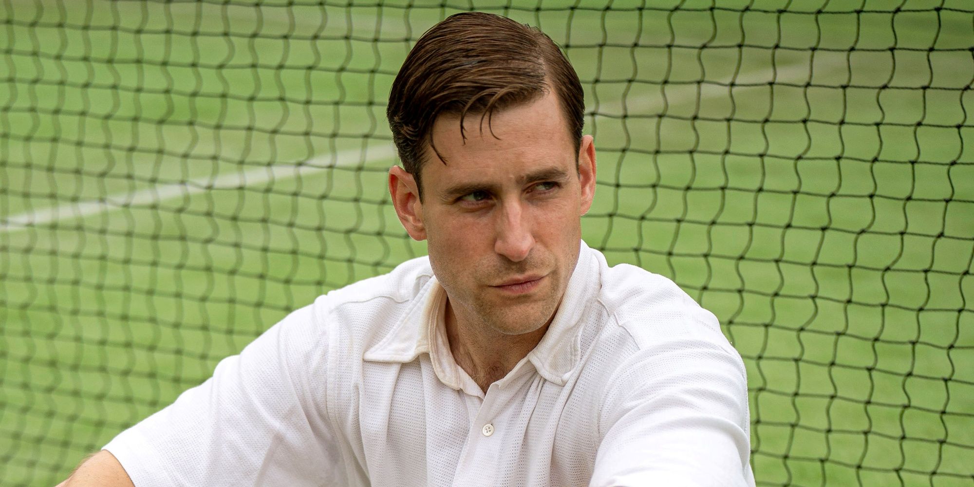 Oliver Jackson-Cohen as Neville Strange sitting against a net on a tennis court in Towards Zero