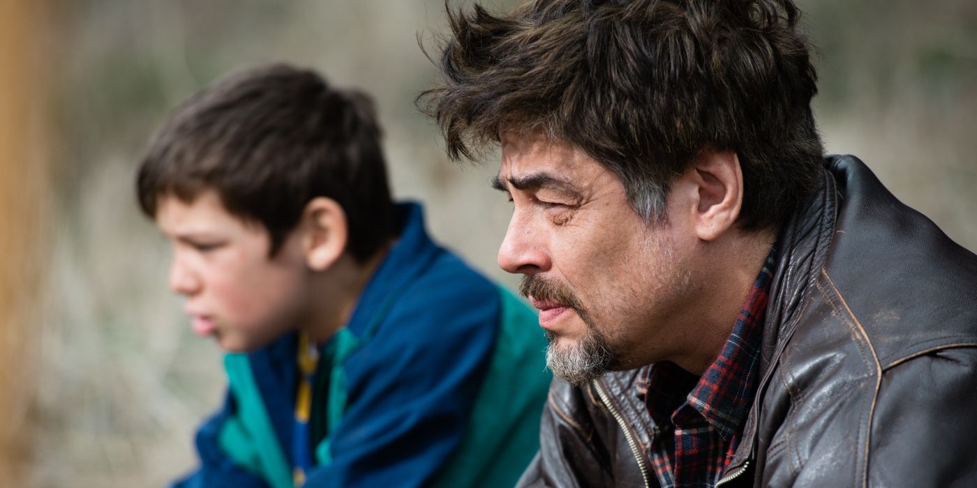 Benicio del Toro and Eldar Residovic sitting and looking at something off-screen to the left in A Perfect Day