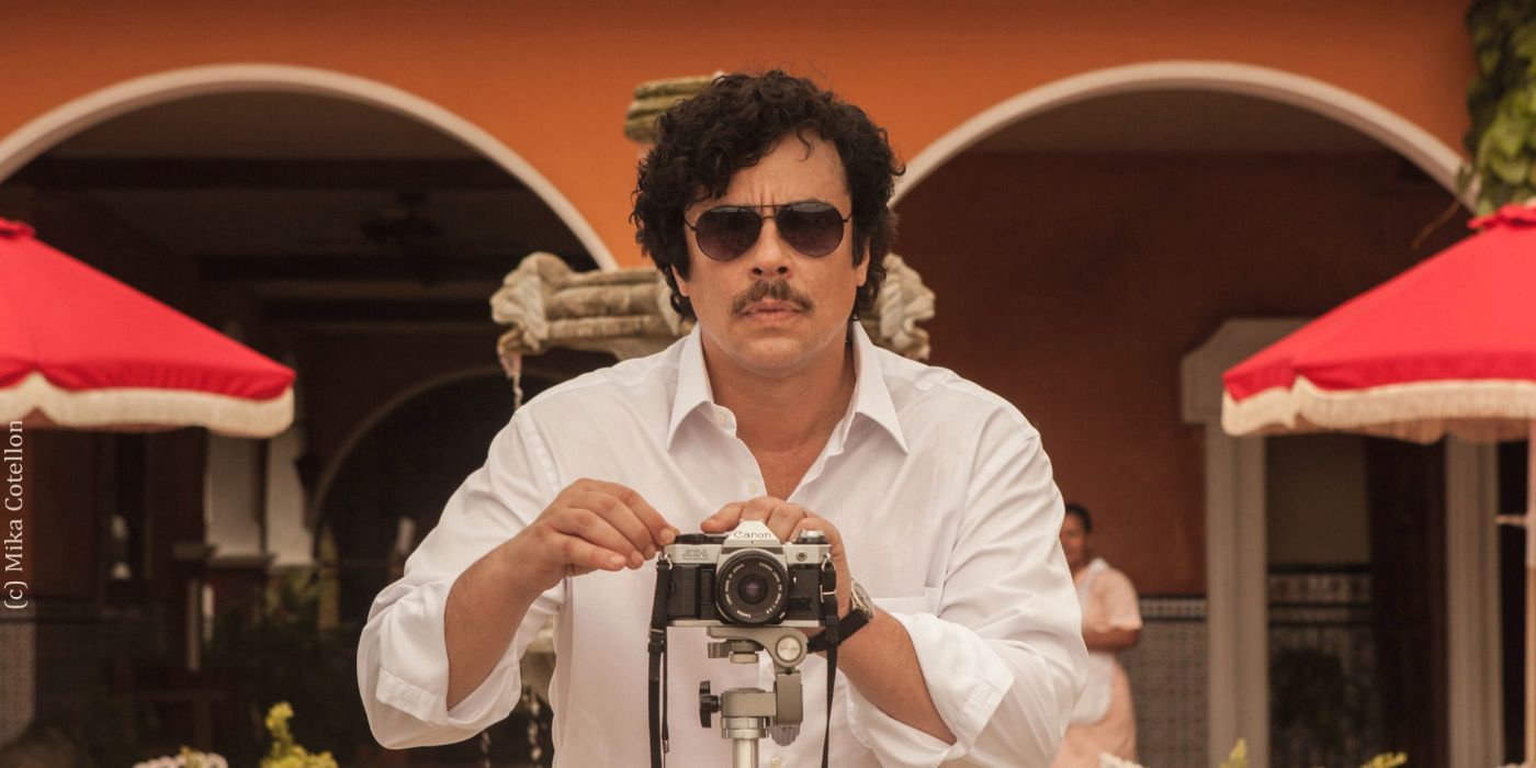 Benicio del Toro as Pablo Escobar taking a photo with a camera in Escobar: Paradise Lost
