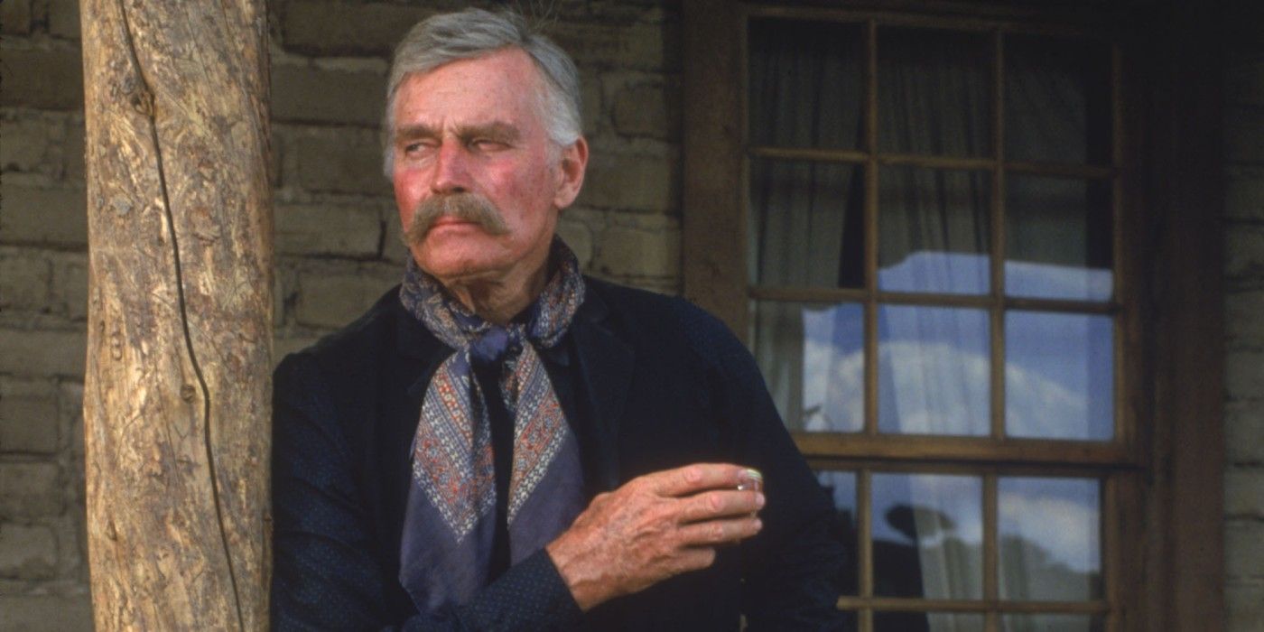 Charlton Heston as Henry Hooker leans against a doorway with a cigarette in Tombstone