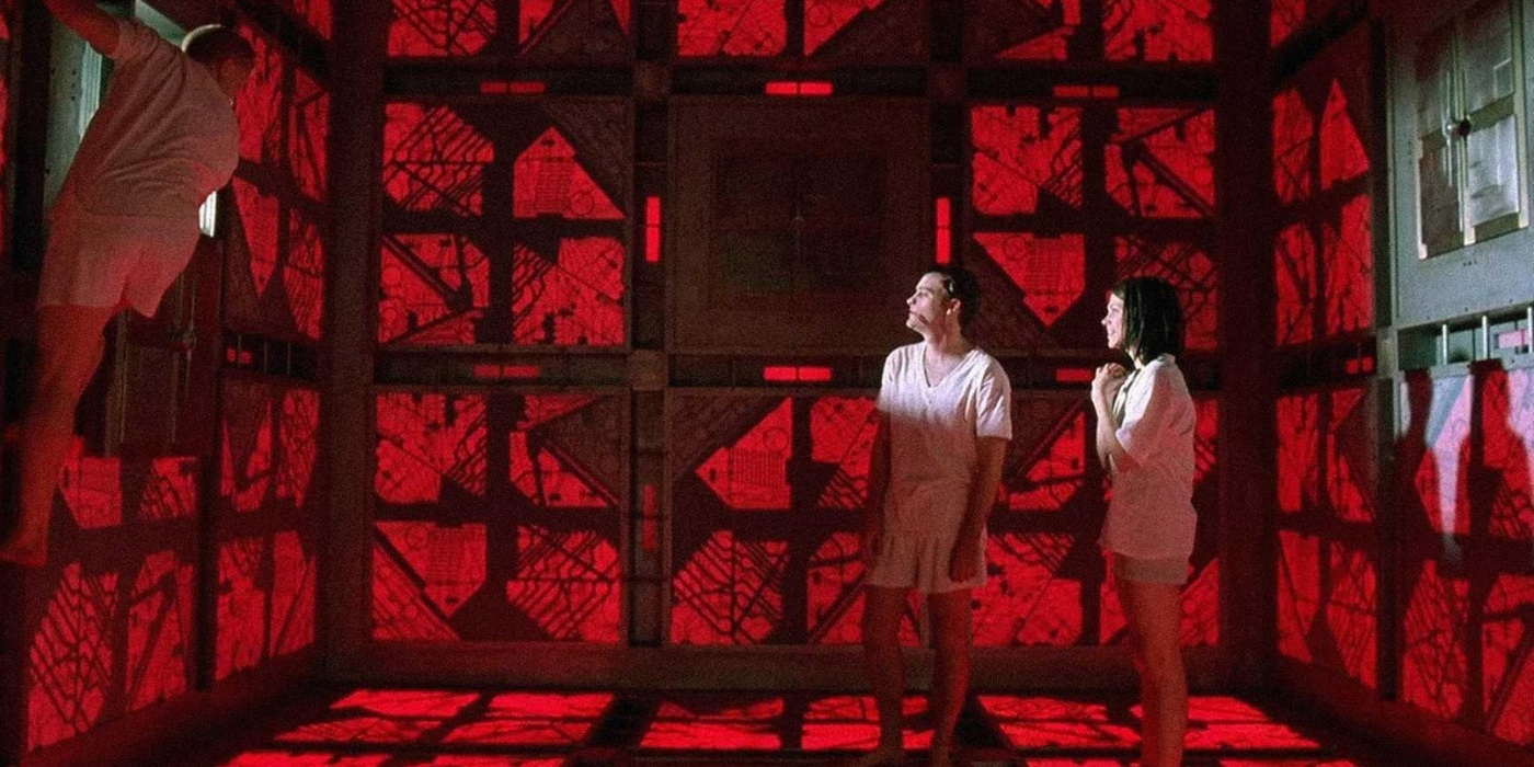 Three people are inside a cube shaped room with white T-shirt and pants