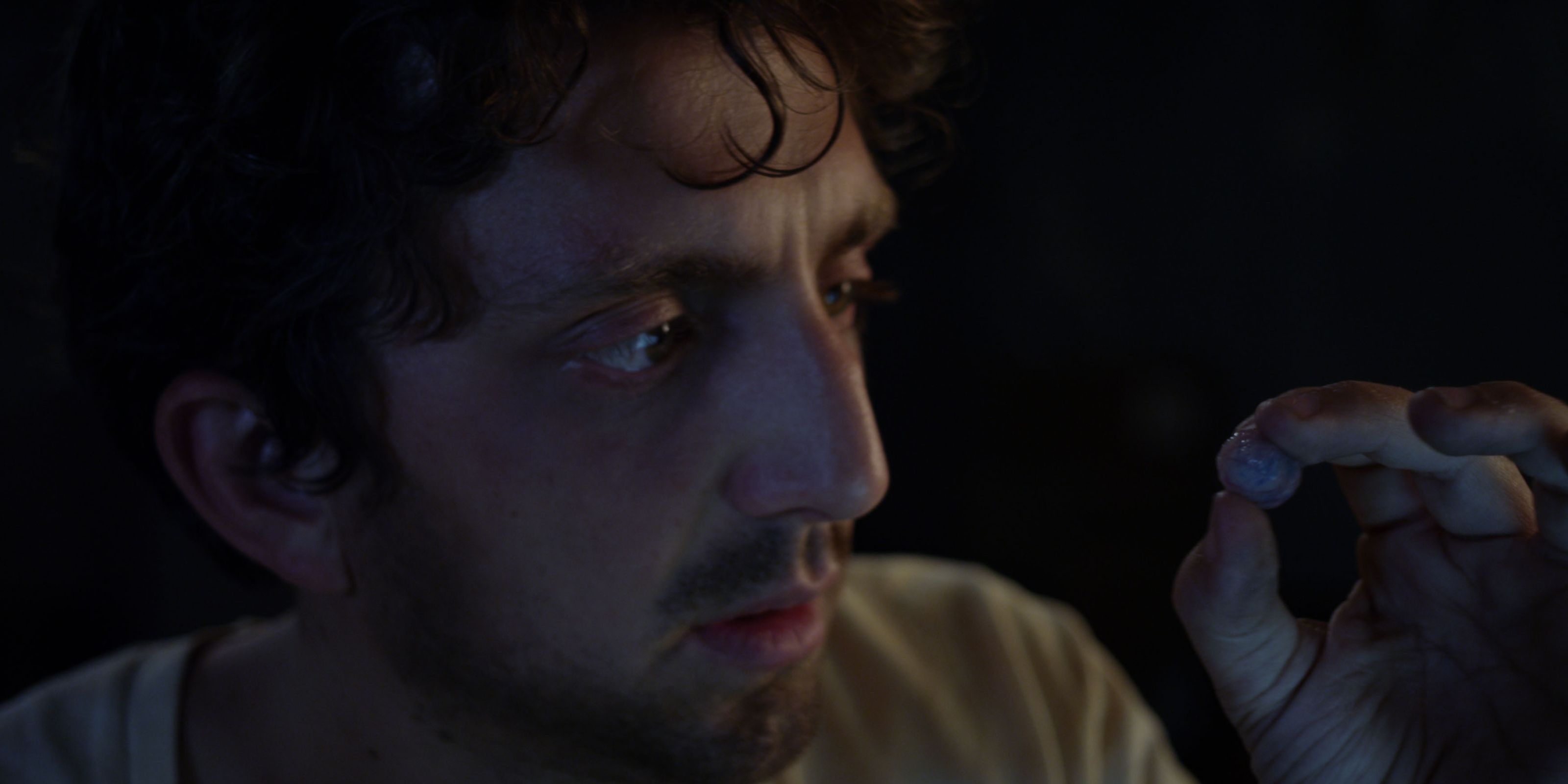 Hermann, played by actor Sean McGrath, looks intently at his own hand, his thumb and index finger connected into a circle in Deep Dark.