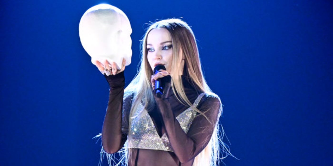 Dove Cameron holding a head made of clay while singing &ldquo;Too Much&rdquo;.