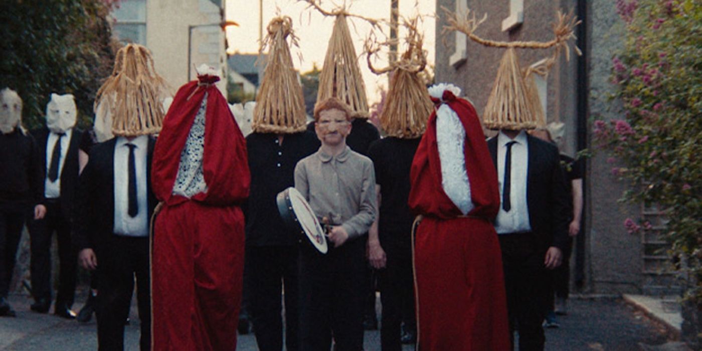 A young boy in a mask surrounded by people in costumes and woven hats in Frewaka