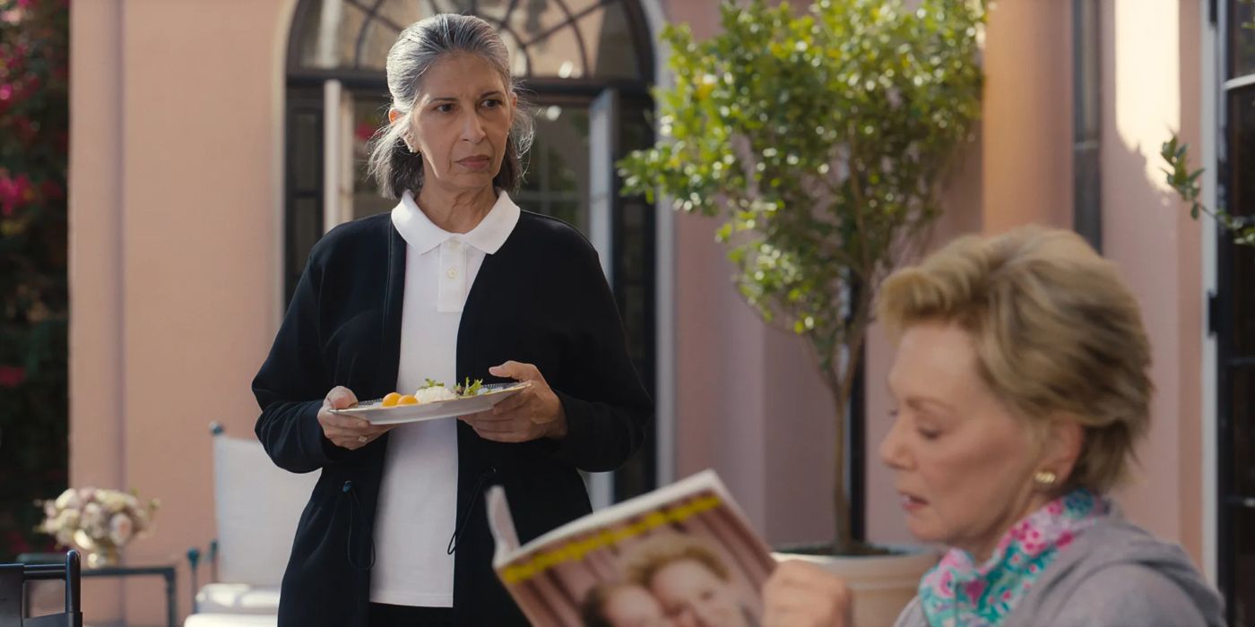 Rose Abdoo as Josefina standing over Jean Smart as Deborah and holding a plate of food in Hacks.