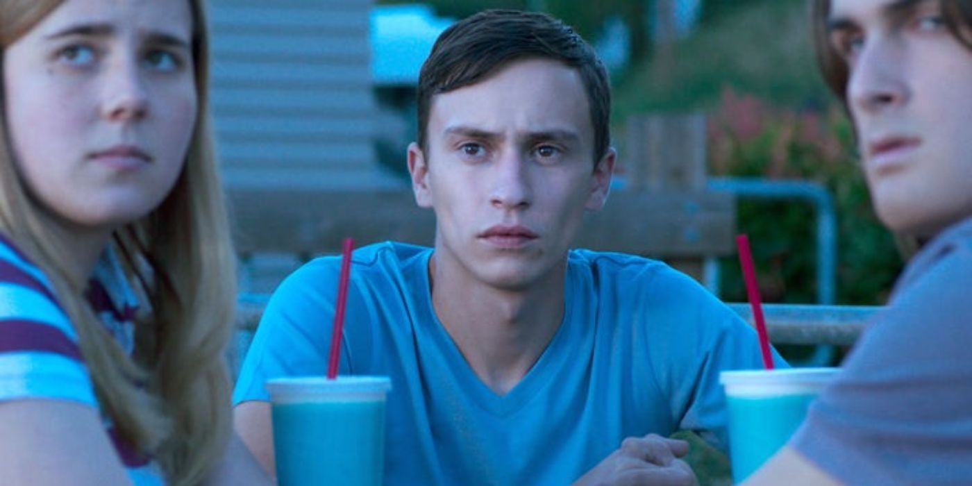 Keir Gilchrist as Henry sits at a table with others, looking at something off-camera in Heartthrob.