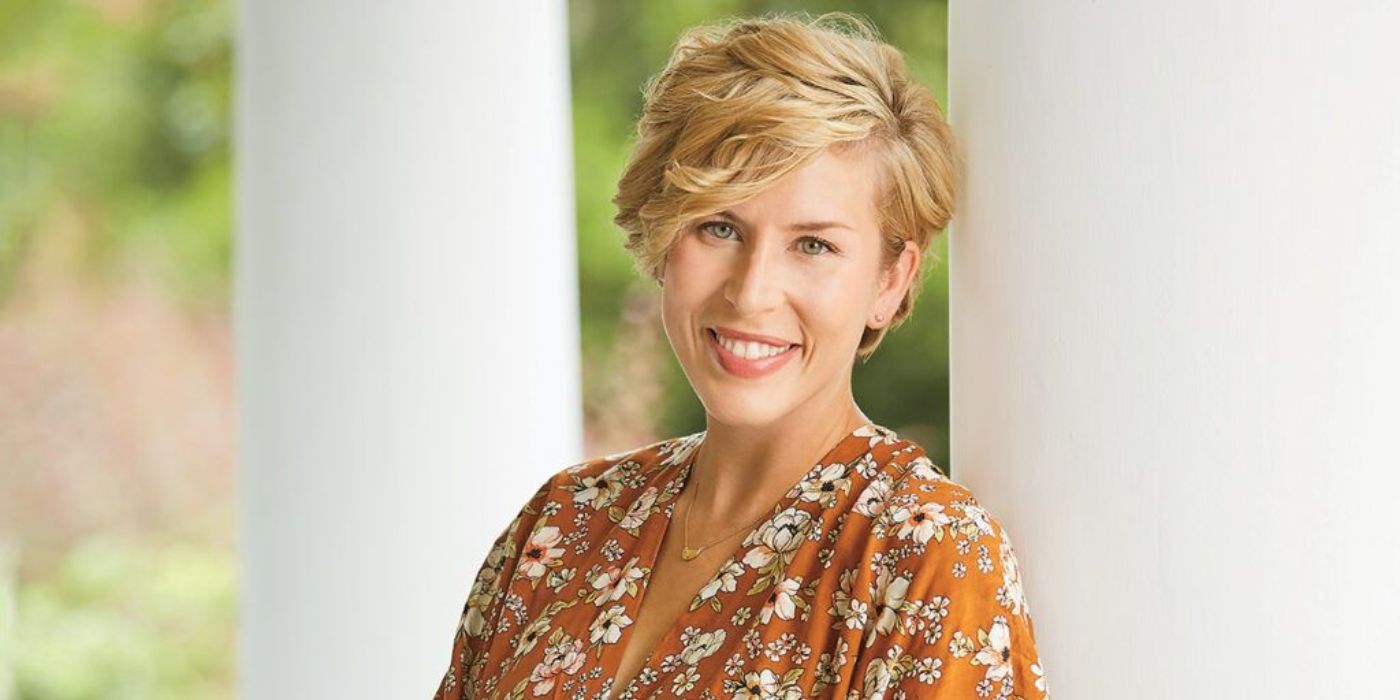 Erin Napier&rsquo;s promo photo for Home Town, as she smiles and leans against a white column outdoors.