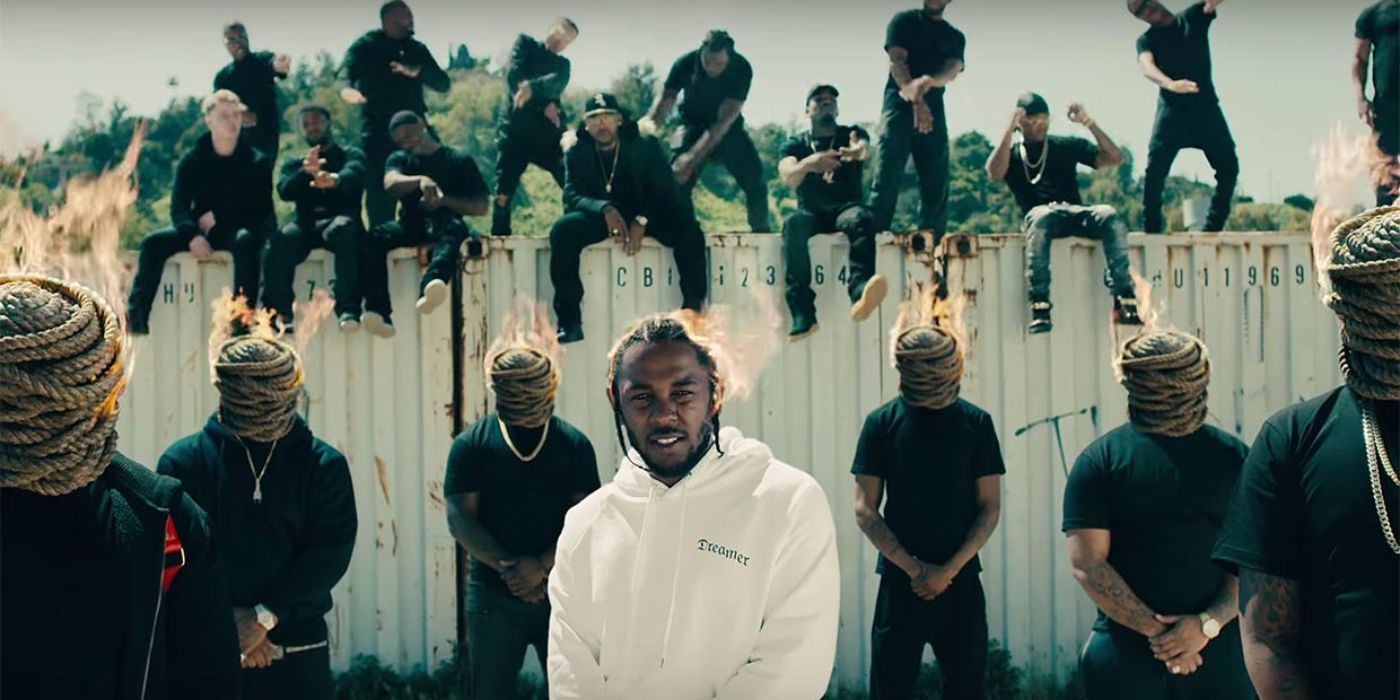 Kendrick Lamar stands in the center surrounded by men dressed in black with burning ropes on their heads