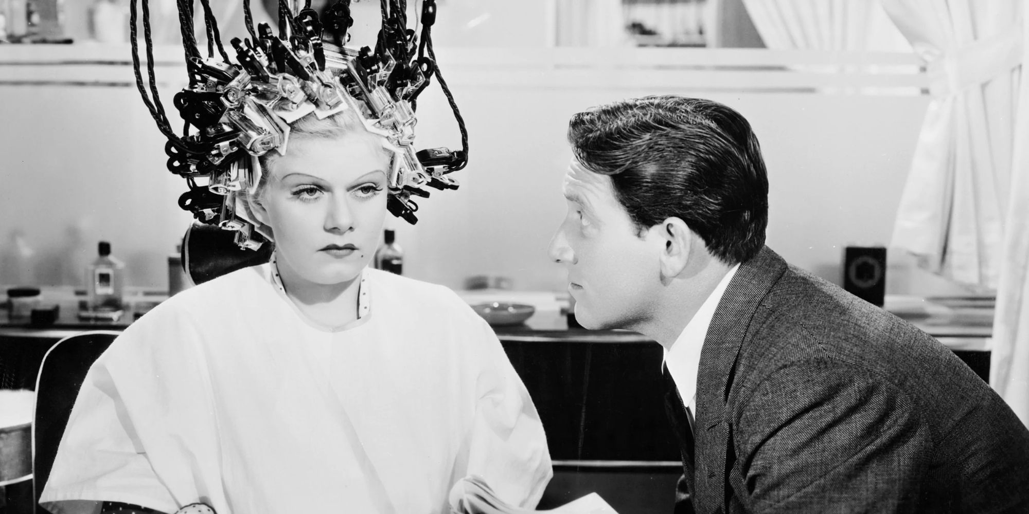 Jean Harlow sits in a salon chair with rollers as Spencer Tracy sits next to her in Libeled Lady, 1936.