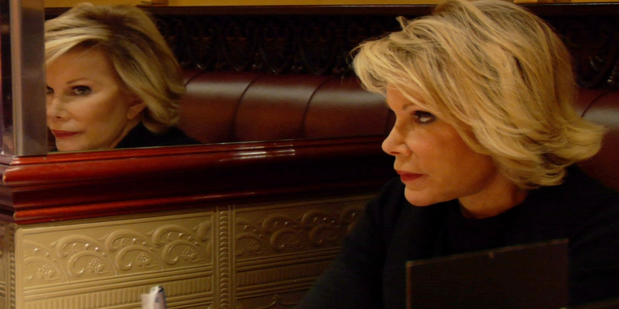 Joan Rivers in a restaurant booth looks at her reflection in the mirror wall in Joan Rivers: A Piece of Work.