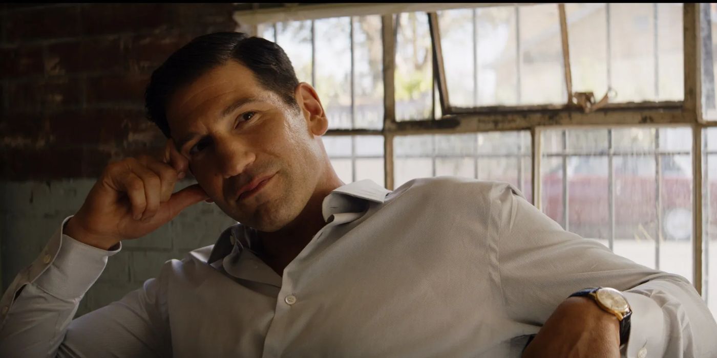 Jon Bernthal as Lee Iacocca leaning on a chair and smiling in Ford v Ferrari.