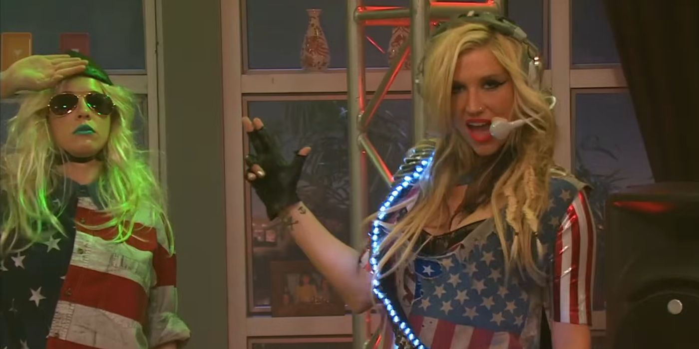 Kesha wearing a flashy United States flag costume and singing into a headset microphone with one of her backup dancers (also wearing an American flag) standing next to her on &ldquo;Victorious.&quot;