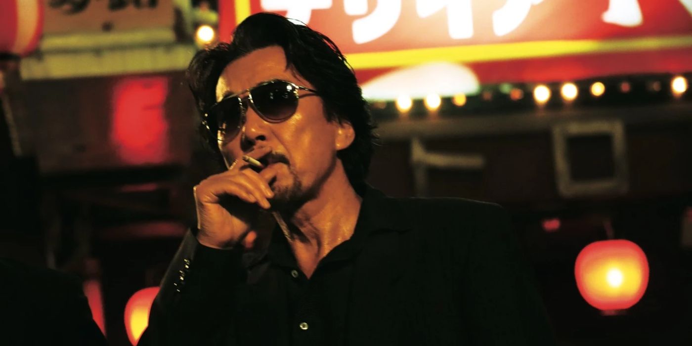 Koji Yakusho as Ogami wearing sunglasses indoors and taking a drag of a cigarette in The Blood of Wolves