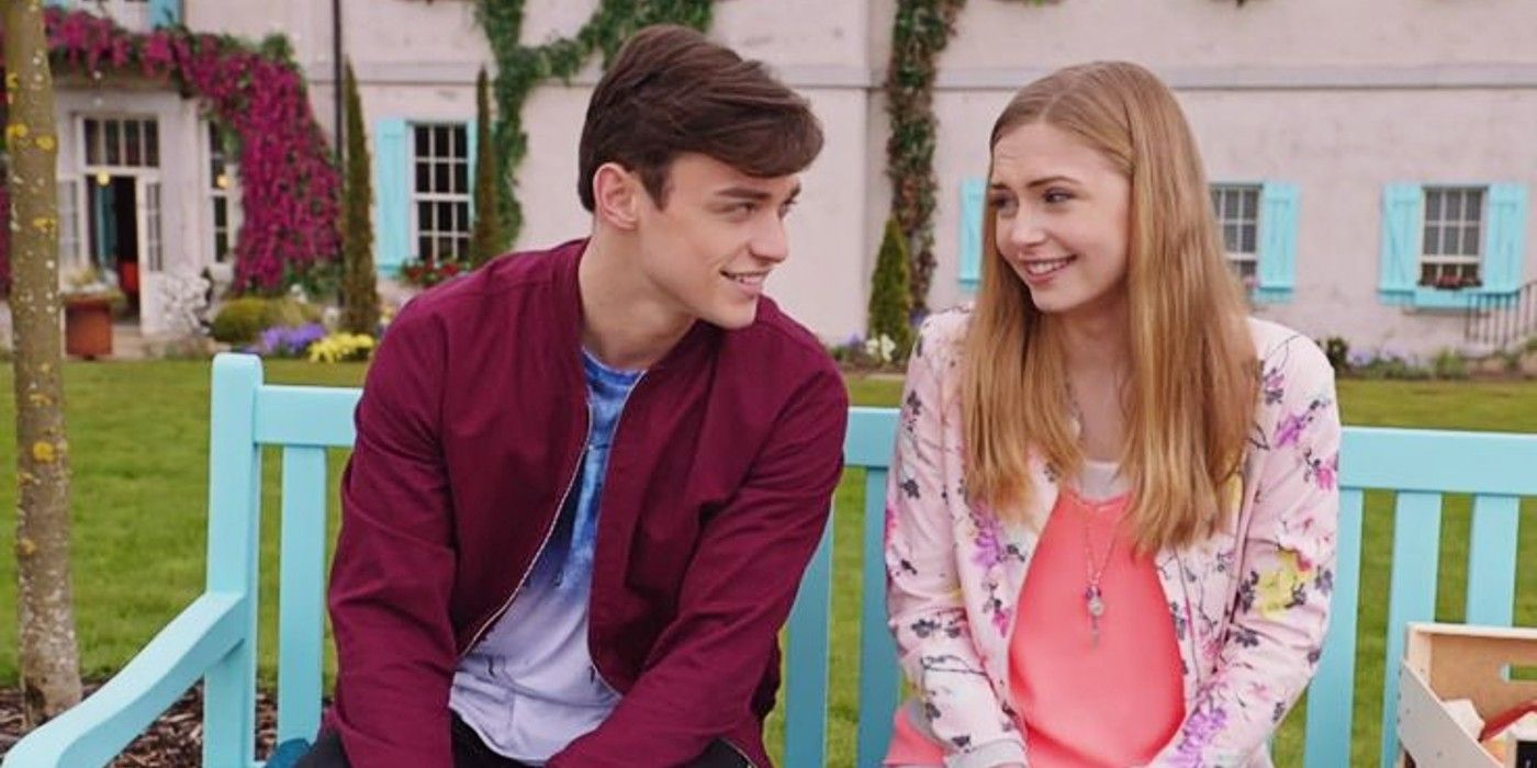 Sean and Skye sit next to each other on a bench outside and smile in The Lodge.