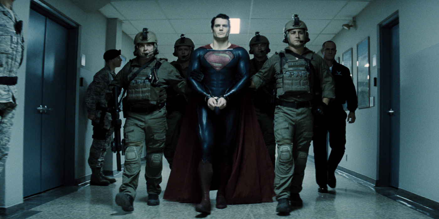 Superman is handcuffed and escorted by a group of soldiers in a hallway