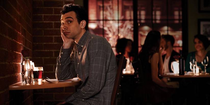 Jay Baruchel as Josh Greenberg sits alone at a table in a dark bar with a drink in Man Seeking Woman. 
