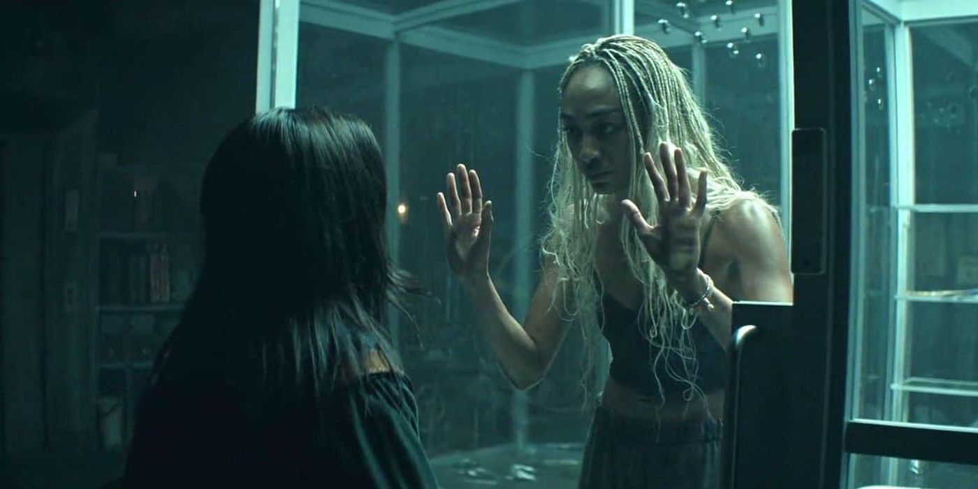 Tati Gabrielle, who is trapped in a glass cage, stares intensely at Amy-Leigh Hickman, who&rsquo;s facing away from the camera, in You Season 4