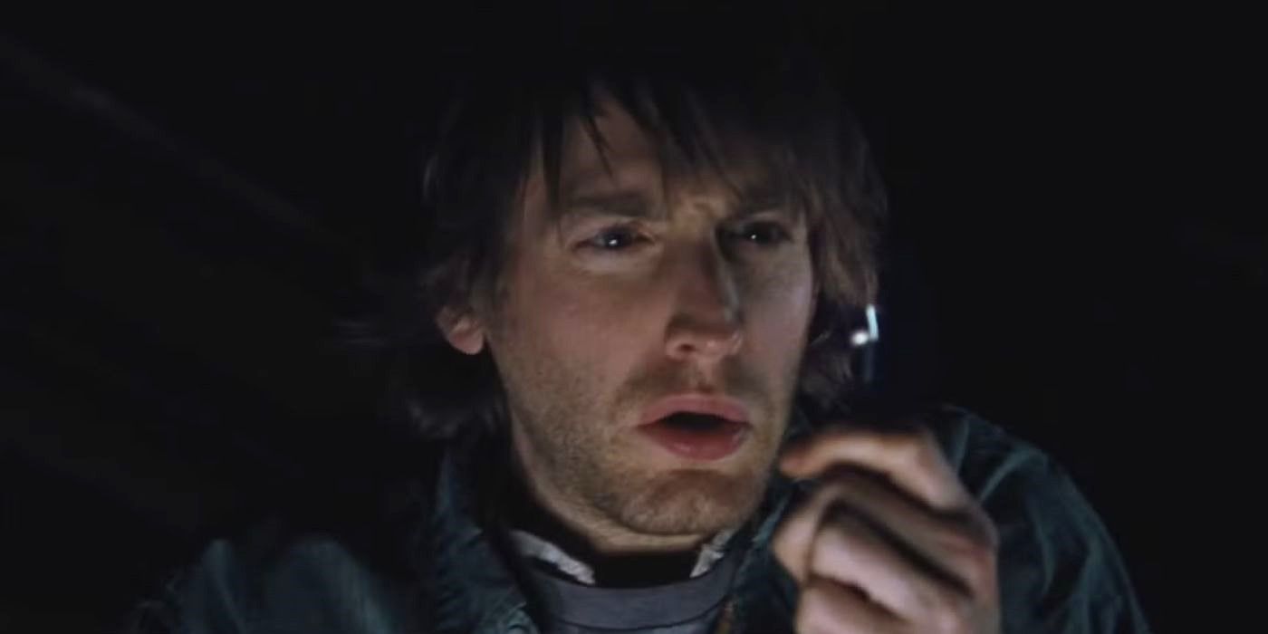 Marty sits alone in the dark looking puzzled in The Cabin in the Woods.