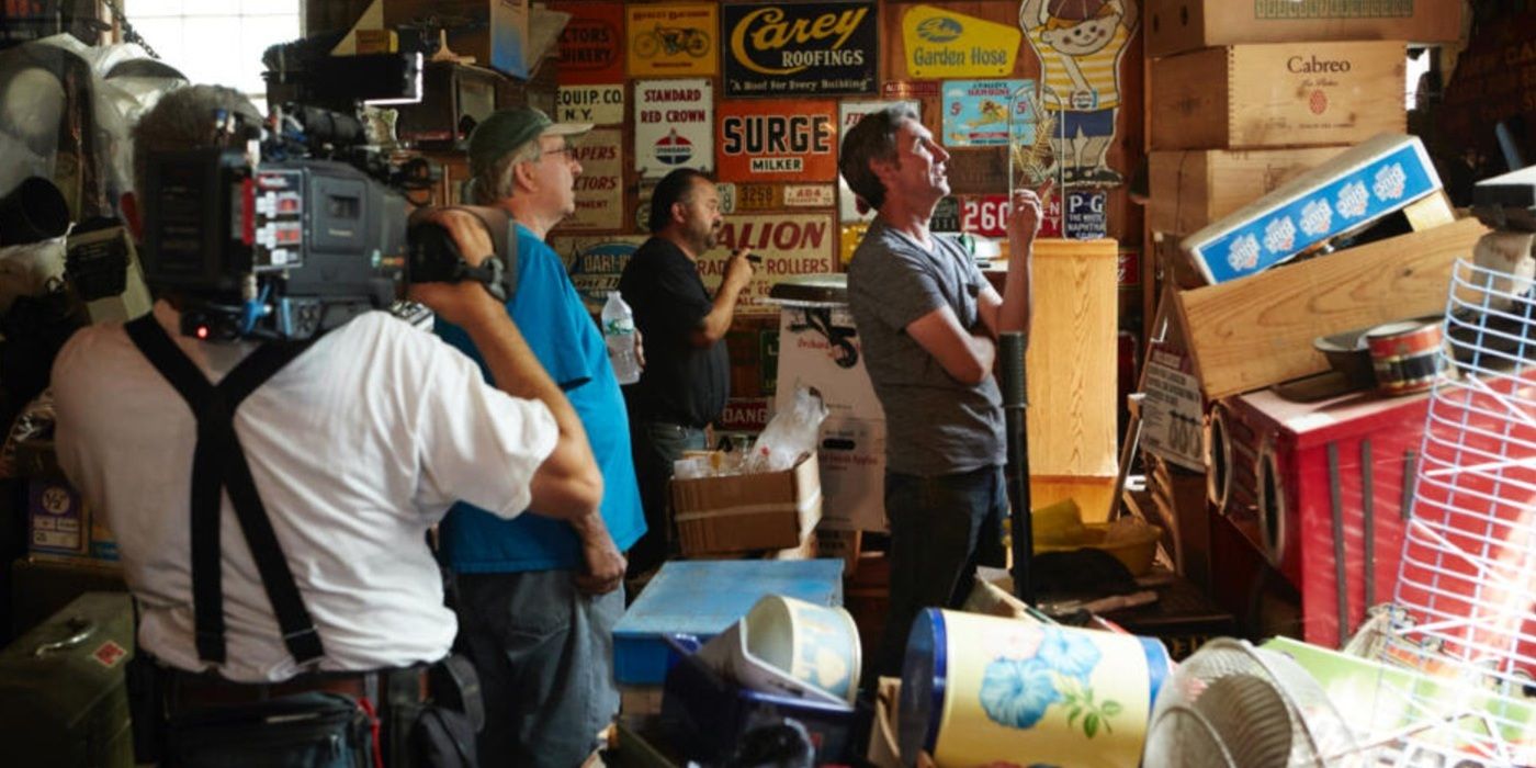 A cameraman films as Mike Wolfe stands in a room full of boxes and memorabilia on American Pickers.