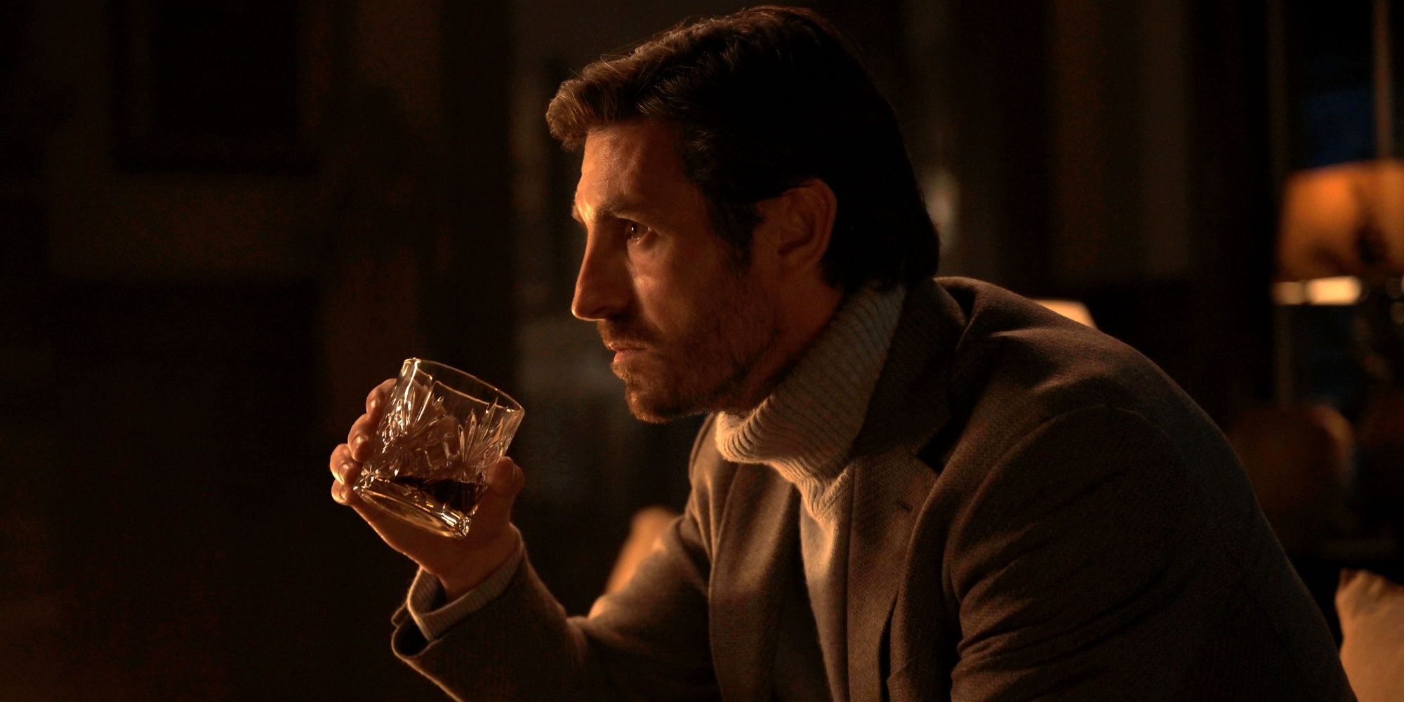 Eoin Macken as Davis Collins sitting and having a drink in a turtleneck and blazer in Ransom Canyon
