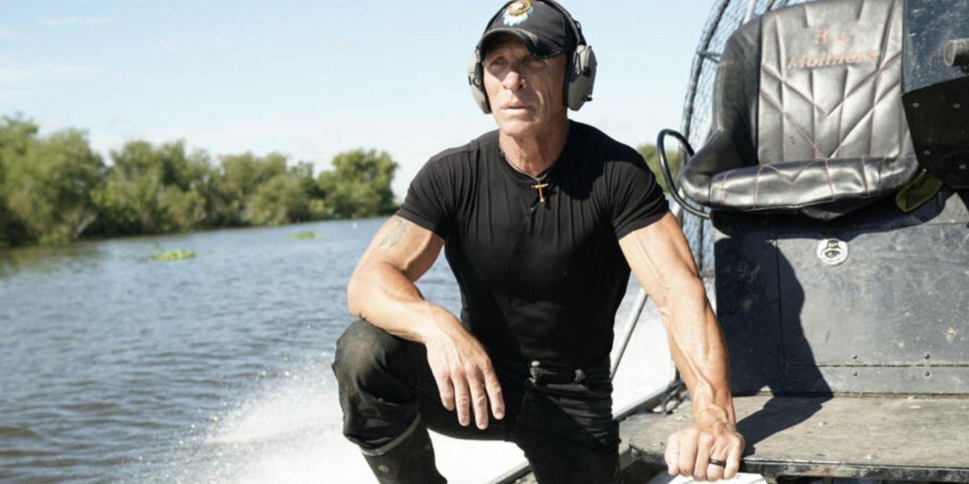 R.J. Molinere wearing a cap and ear protectors on an airboat on water in the bayou in Swamp People.
