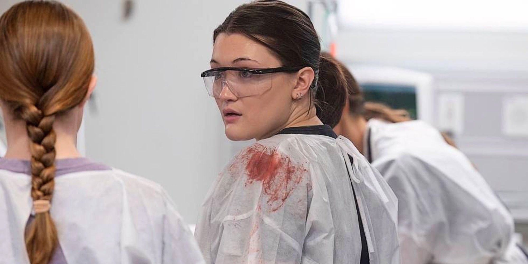 Santos in bloody scrubs and safety glasses talking to Mel in The Pitt Season 1.