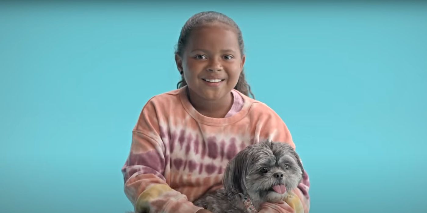 A young girl smiles at the camera in front of a blue backdrop while holding a dog in the Disney+ documentary, Pets