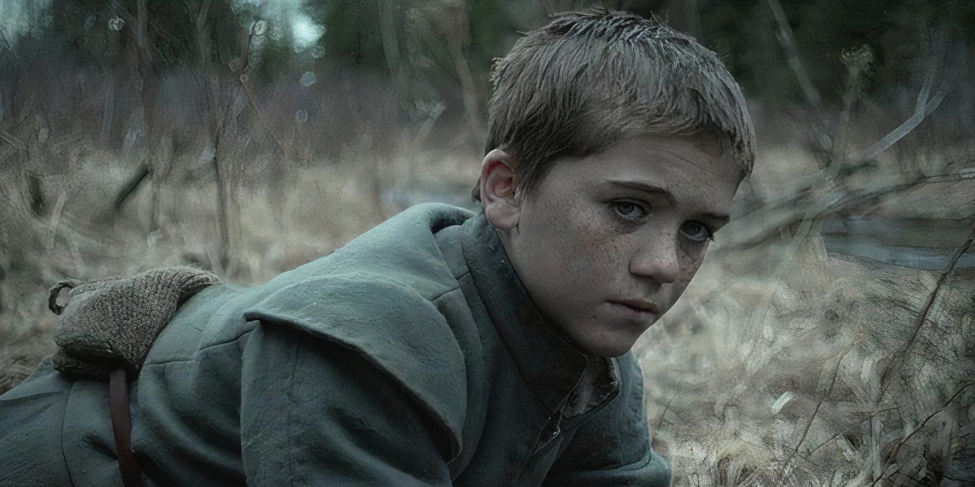 Harvey Crimshaw as Caleb in The Witch leans down in a field as and looks thoughtfully towards the camera.