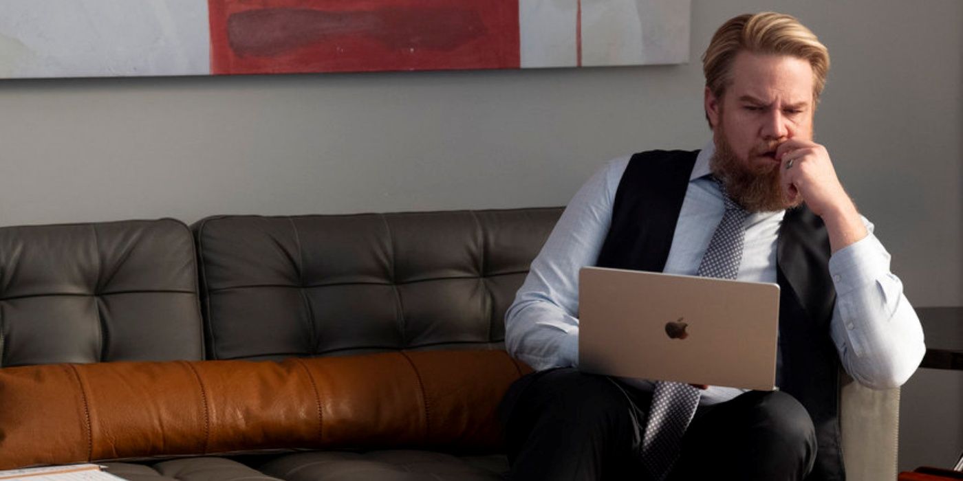 Josh McDermitt as Stuart Lane sitting on a couch with his laptop on his lap in Suits LA