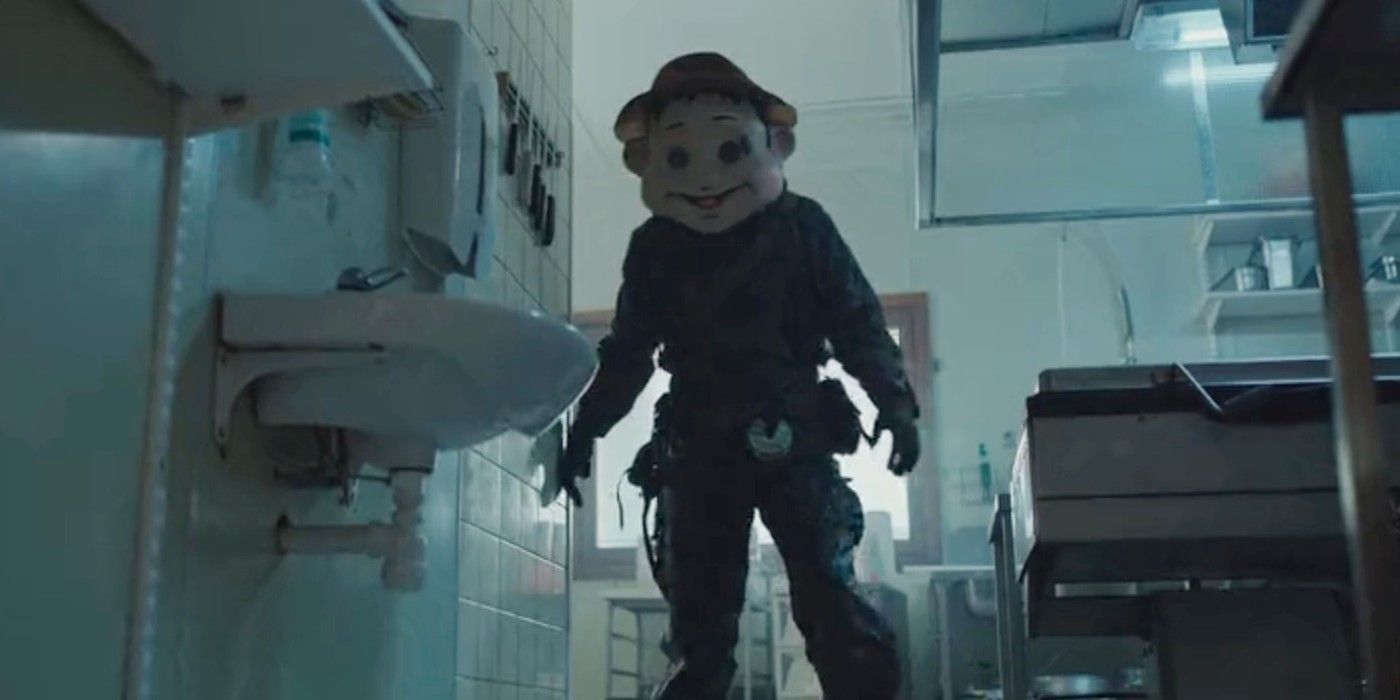 A man wearing wilderness gear and the large mascot head of a cartoon Swedish person in The Conference.