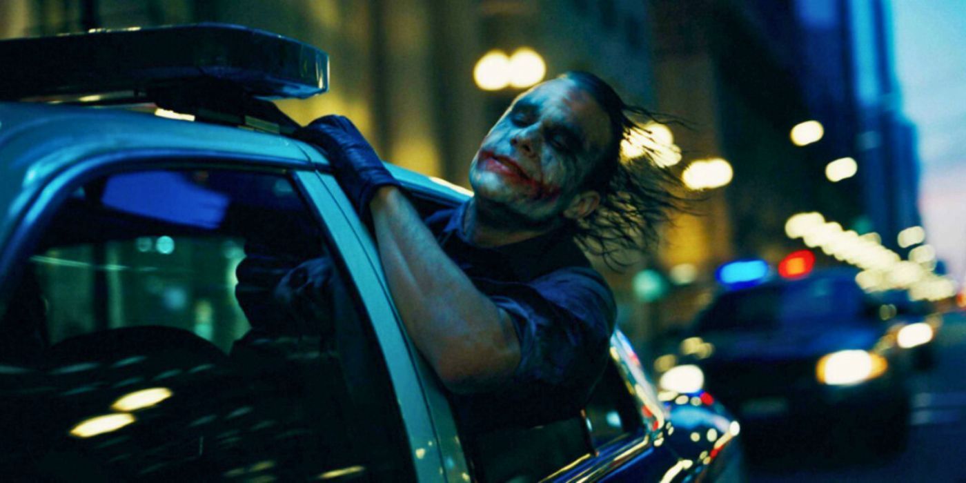 Heath Ledger as The Joker leans out of the window of a moving police car in The Dark Knight