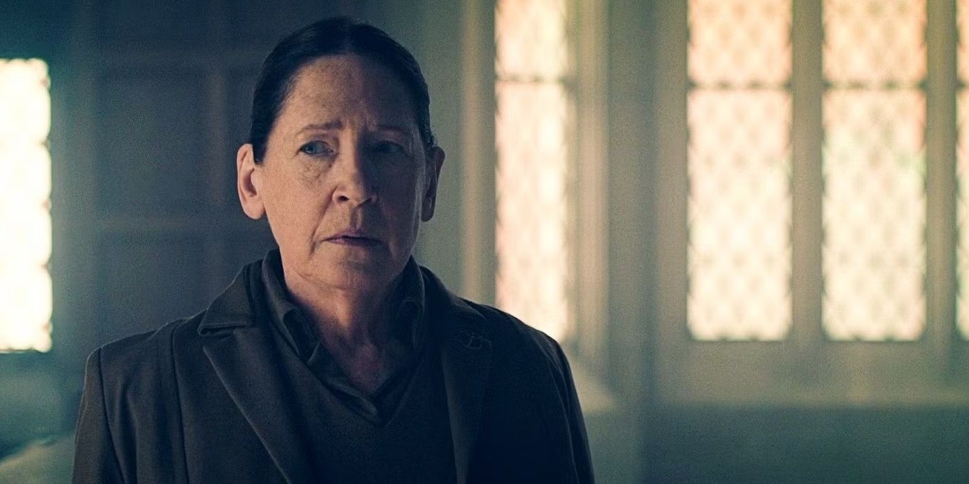 Ann Dowd como tia Lydia, olhando para fora da câmera com preocupação, em um imóvel da história das criadas.