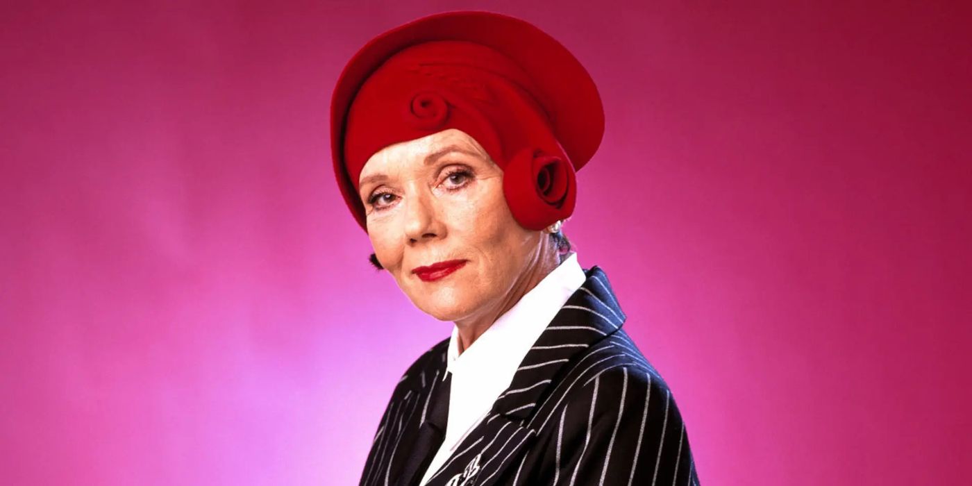 Mrs Bradley (Diana Rigg) standing in front of a red background and smirking in The Mrs Bradley Mysteries.