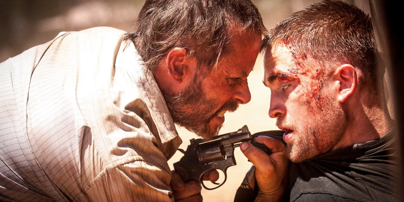An angry Guy Pearce points a gun at bruised Robert Pattinson