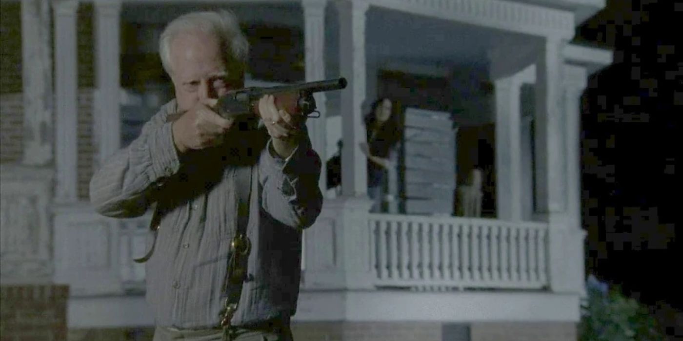 Hershel aims a shotgun at something off-camera as he stands outside a house at night in The Walking Dead.