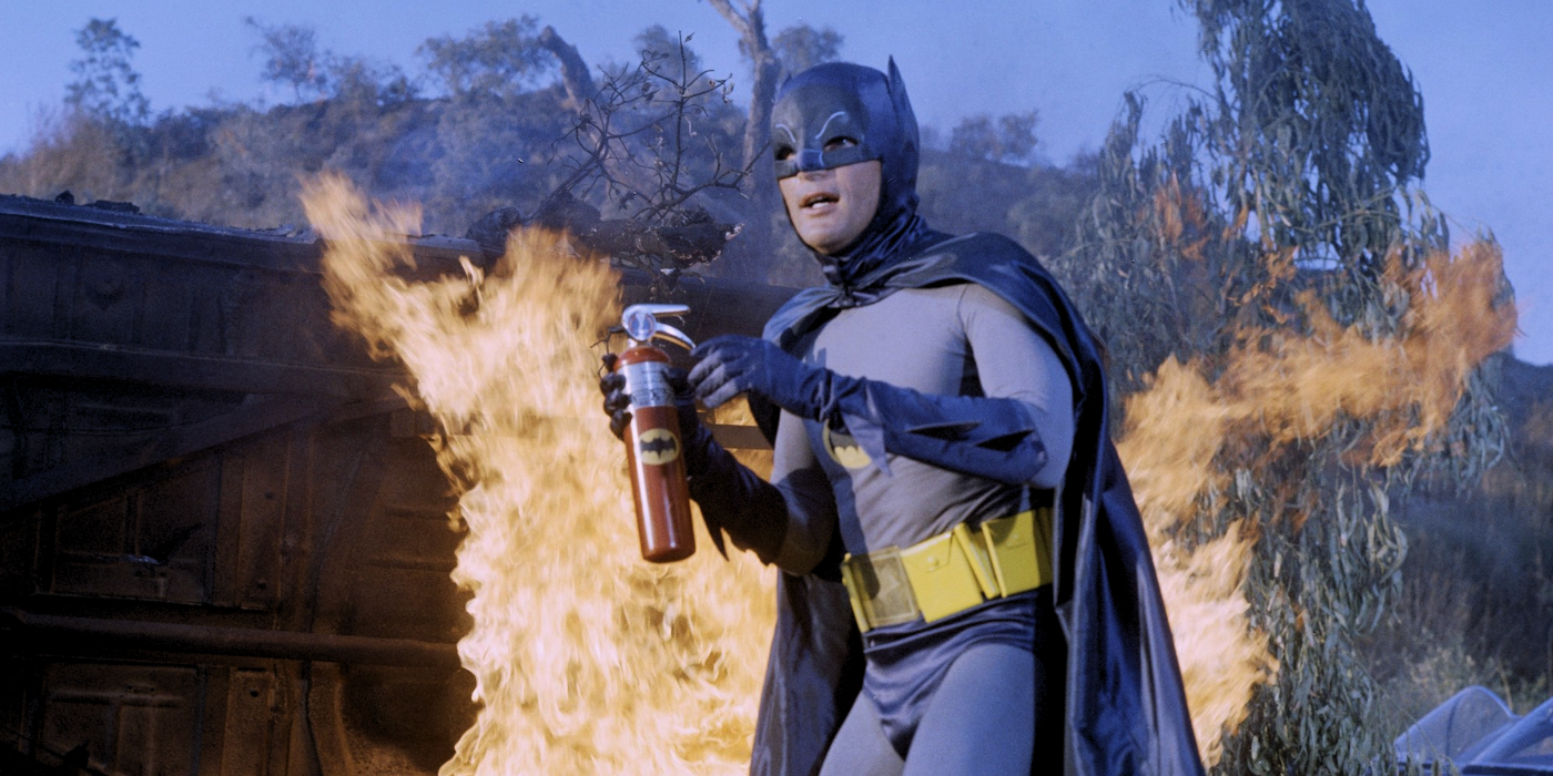 Adam West as Batman brings his fire extinguisher as he stands in front of fire in Batman.