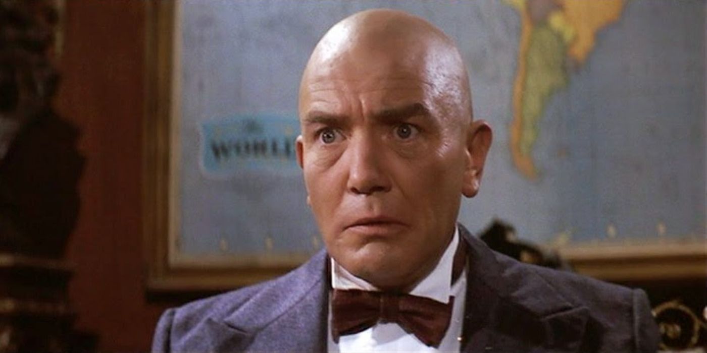 Albert Finney with a bald head as Daddy Warbucks in Annie looking confused in a suit and bow tie.