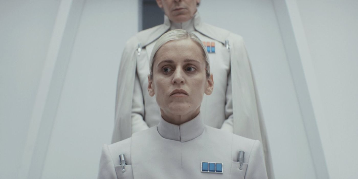 Krennic (Ben Mendelsohn) looming behind a sitting Dedra Meero (Denise Gough) in Andor